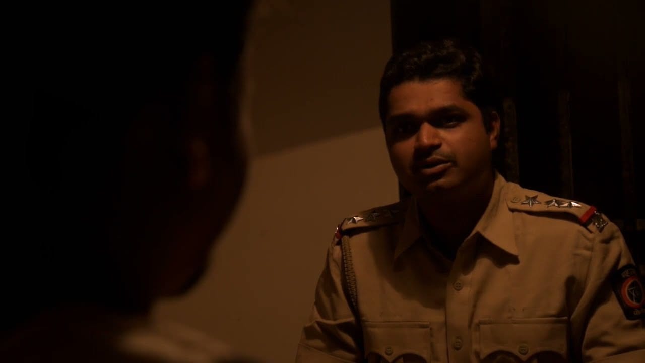 A police officer speaks with someone in a dim interior, a frame from Aarakshan